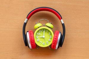 Headphones and alarm clock on wooden desk. Musical concept photo