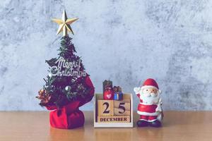 fecha del calendario del bloque 25 de diciembre calendario y decoración navideña - santa claus, árbol y regalo en la mesa de madera. concepto de navidad y feliz año nuevo foto