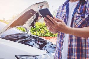 hombre de asia parado frente a un auto roto pidiendo ayuda foto