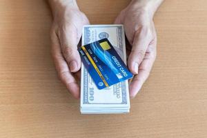 manos de hombre sosteniendo billetes de 100 dólares y tarjeta de crédito en una mesa de madera. concepto financiero foto