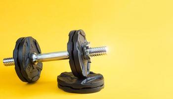 Dumbbell with disks on a yellow background close-up. Sports lifestyle, strength training, gym. Copy space photo