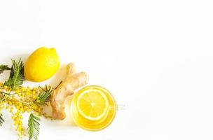 Herbal tea in a cup, ginger, lemon and acacia - strengthen immune system in the cold season. Allergies, fever, flu. Vitamin drink for health and ingredients on a white background. Copy space, flatly photo