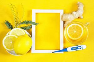 Medicinal tea in a cup, ginger, lemon, acacia-strengthen the immune system in cold season, thermometer and copy space, sheet for notes. Vitamin drink for health and ingredients on yellow background. photo