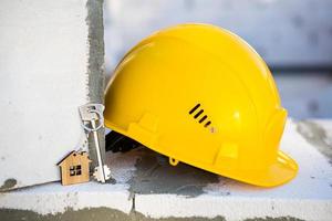 Construction yellow hardhat and key to house on window of housing made of blocks of porous concrete. Turnkey construction, future home, engineering, building. Work safety. Copy space photo