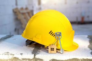 Construction yellow hardhat and key to house on window of housing made of blocks of porous concrete. Turnkey construction, future home, engineering, building. Work safety. Copy space photo