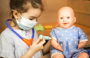 A girl with a doll plays doctor, makes a syringe inoculation in the hand. Vaccination, vaccination calendar, vaccine, profession game. Nurse's injection photo