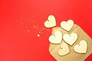 los corazones de madera se derraman de un sobre abierto sobre un fondo rojo. día de san valentín, carta de amor, declaración de amor, conocido. copia espacio, maqueta foto