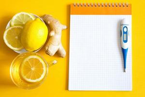 Medicinal tea in a cup, ginger, lemon-strengthen the immune system in the cold season, thermometer and copy space, sheet for notes. Vitamin drink for health and ingredients on yellow background. photo
