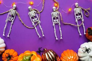 Halloween layout of garland of skeletons on a rope, glowing Jack o Latern, pumpkins, spiders on a purple background. Flat lay horror and a terrible holiday photo