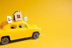 Yellow toy car with a key to the house on the roof on a color background. Moving to a new home, mortgage, buying an apartment, taxi. Copy space. photo