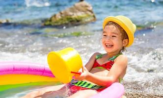 chica con sombrero de paja amarillo juega con el viento, el agua y un dispensador de agua en una piscina inflable en la playa. productos indelebles para proteger la piel de los niños del sol, las quemaduras solares. recurso en el mar. foto