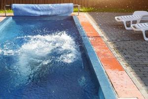 Splashes in the outdoor swimming pool near the white deck chairs. Recreation area at the resort, ticket to the hotel, sauna and spa, sports and swimming. Copy space photo