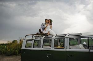 Hipster bride and groom are standing near their retro bus. photo