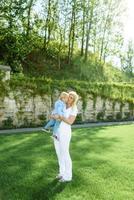 Mom leads her son's hand through the green grass. Both blondes. photo