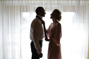 Gorgeous, blonde bride in a white luxurious dress getting ready for the wedding. Morning preparations. A woman puts on a dress. The groom helps the bride. photo