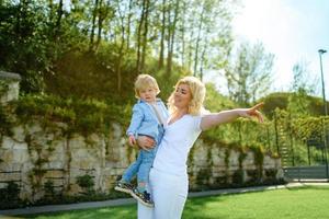 Mom leads her son's hand through the green grass. Both blondes. photo