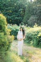 Young pregnant woman in spring lilac blooming garden. Romantic look with straw hat. Caucasian woman with long brown hairs. Concept of new life of nature and human. Waiting of baby