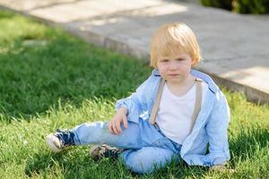 niño rubio se sienta en la hierba verde. foto