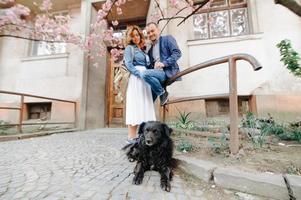 Young Love Couple Hugging their Dog in the Spring Park with Blooming Cherry Tree photo