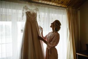 novia en bata de noche sosteniendo su vestido de novia en la sombra foto