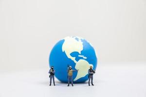 concepto global de defensa y protección. primer plano de un grupo de soldados en miniatura con un arma de pie frente a la mini bola mundial sobre fondo blanco y espacio de copia. foto