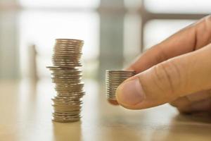 concepto de negocio, ahorro y jubilación. primer plano de la pila de monedas en la mano del hombre poniendo sobre la mesa de madera cerca de la pila inestable de monedas. foto