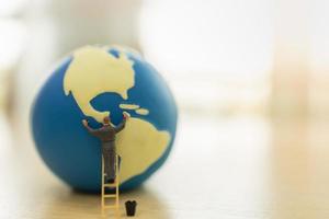 Save Global Environment Care Concept. Close up of worker miniature people standing on stair and cleaning mini world ball with water tank on wooden table with copy space. photo