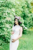 feliz mujer embarazada en una corona y un ramo de flores silvestres o