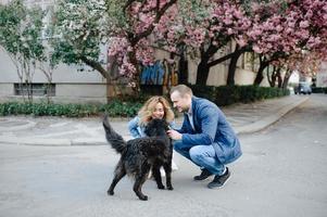 Young Love Couple Hugging their Dog in the Spring Park with Blooming Cherry Tree photo