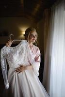 A young cute blonde bride in a bathrobe is trying on her wedding dress. photo