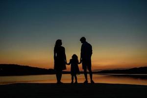 silueta de una familia de tres. los padres arrojan a su hija al cielo. foto