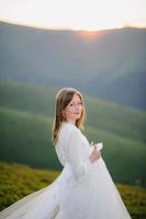 woman in a wedding dress runs across the field toward the mountains photo