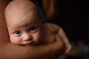 A newborn boy lies in the arms of his mother and looks into the lens. photo