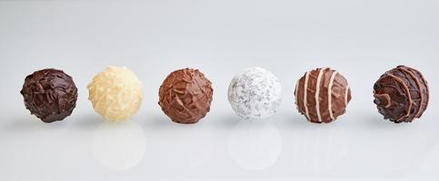 row of six chocolate truffles on white background with reflection