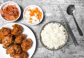 Topview yangnyeom tongdak Korean spicy deep-fried chicken topped white sesame with kimchi and pickled radish side dishes and rice on the gray concrete table, popular street food in Korea. photo