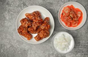 topview yangnyeom tongdak pollo frito picante coreano cubierto de sésamo blanco con kimchi y guarniciones de rábano en escabeche en la mesa de hormigón gris, comida callejera popular en corea. foto