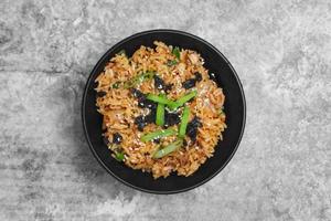 Top view Korean kimchi fried rice topping white sesame and seaweed in a black bowl on the grey concrete table, close-up shot. photo