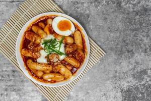 Top view Tteokbokki Spicy Rice Cakes with boiled eggs and cheese on the grey concrete table, Korean street food. photo