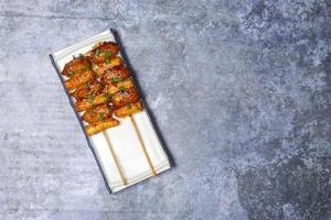 Top view So-tteok is a popular South Korean street food consisting of skewered and rice cake bar and sausage topped with white sesame and green onion leaf. photo