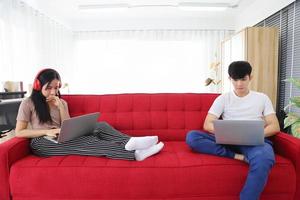 Young Asian couple spending time together on the sofa couch while working online from home with copy space photo
