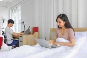pareja joven trabajando en línea desde casa en el dormitorio juntos como cuarentena para una nueva política normal y de distanciamiento social foto