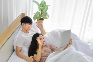 Young Asian couple living in the city make a video call to their parent while lying down on their bed