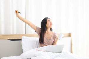 Asian woman stretching after working from home using laptop computer while drinking coffee with copy space