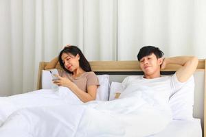 Asian couple laying on the bed in the morning while the wife is checking news from social media using mobile smartphone photo
