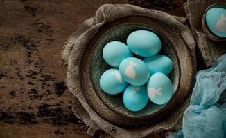 Unusual Easter on dark old background. Ceramic brown bowl with blue eggs with rabbit. photo