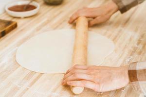 Faceless woman roll out dough with rolling pin on kitchen table at home, photo