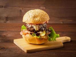 Big delicious homemade burger with beef cutlet, cheese, onion, tomato and lettuce on toasted rolls. American fast food, unhealthy eating. Side view. photo