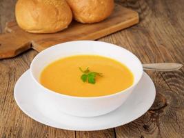 white bowl of pumpkin soup, garnished with parsley on wooden background, side view. photo