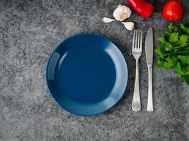 Limpie el plato azul oscuro vacío, el tenedor y el cuchillo sobre fondo de hormigón gris, vista superior. foto