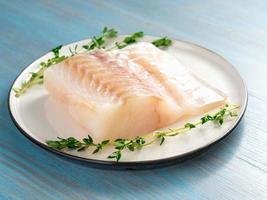 piece of raw cod fish fillet on plate on blue wooden table, side view photo